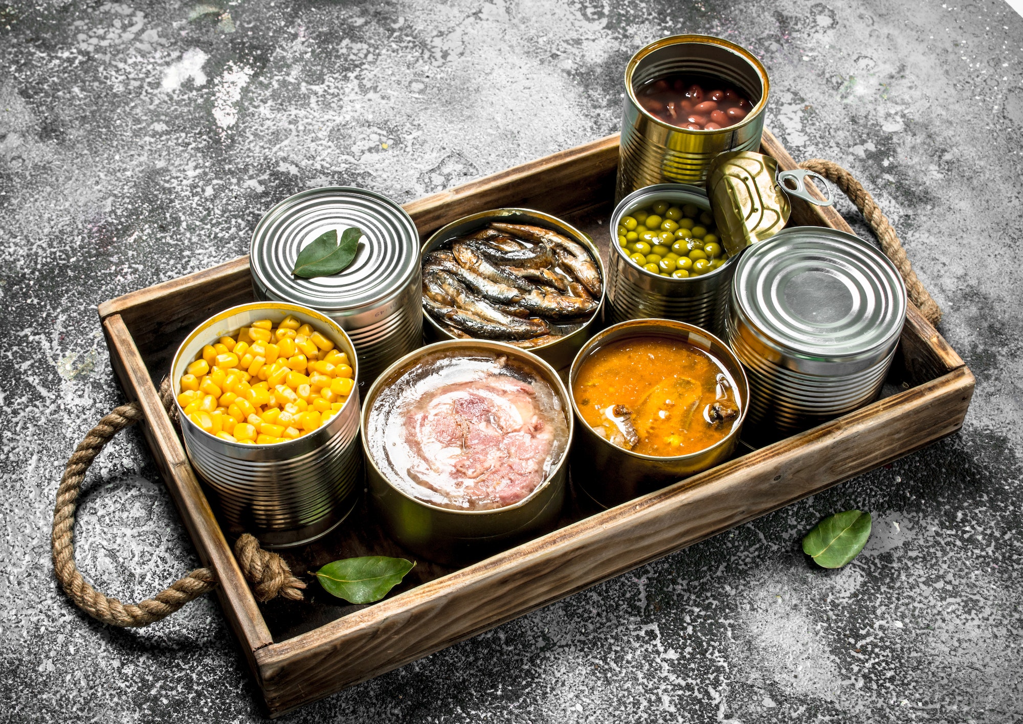 Various canned products in tin cans on a wooden tray.